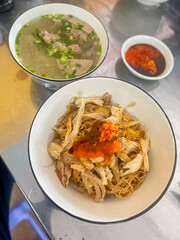 Gia Lai dry pho has shredded chicken, spicy chili sauce, and a bowl of soup consisting of beef and beef balls with onions.