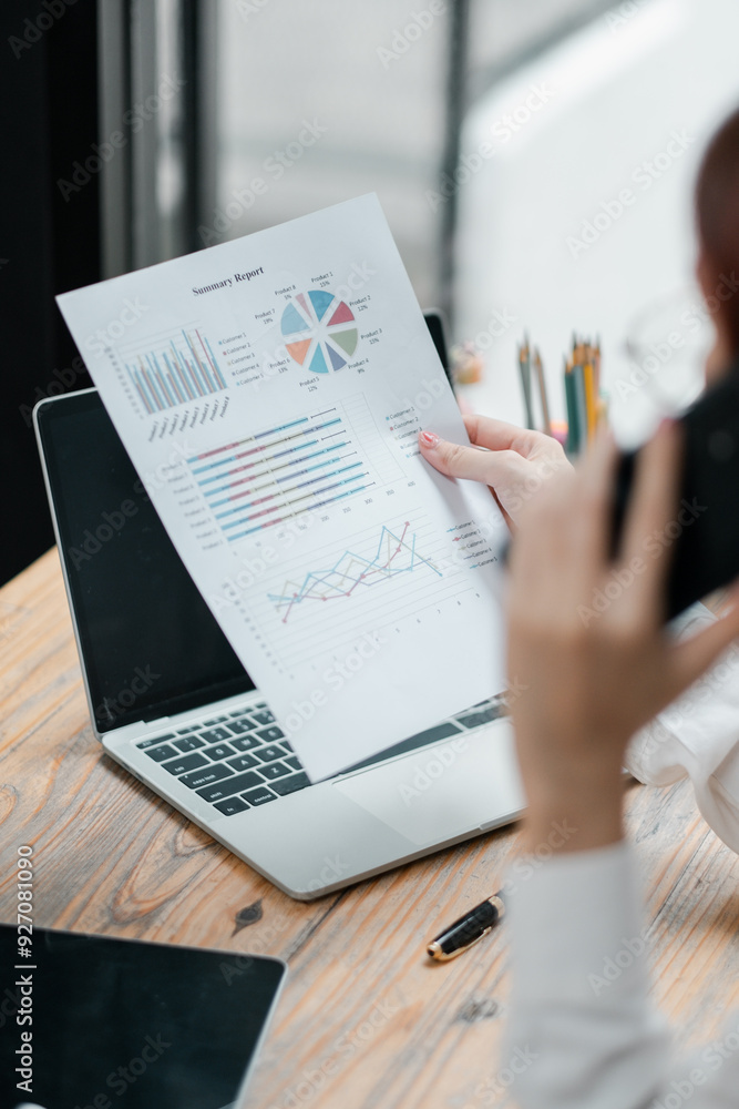 Poster a businesswoman reviews a financial report with various graphs and charts while working on a laptop 