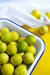 Limes in white tray and wavy white fabric placed on yellow background. Vertical fresh food image. Minimal, home kitchen, sour ingredients, and healthy concept. Yellow limes with yellow and white theme