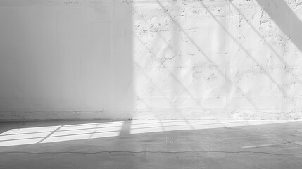 Obraz premium The image shows a wide shot of an empty room, with a concrete floor and a white wall. Light from an unseen window is casting long, diagonal shadows on the floor and wall.