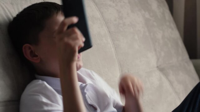 concept of joy of boy using phone, caucasian boy 10 years old looking at smartphone screen and surprisedly happy sitting on sofa at home