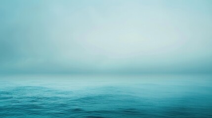Obraz premium A wide, open body of water appears tranquil beneath a sky veiled in a thick haze, the sun just starting to rise, casting a soft, blue light over the scene. Gentle waves roll across the ocean, creating