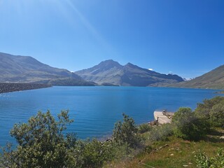 Naklejka premium Cette image panoramique met en valeur le barrage du Mont-Cenis, un ouvrage d'art impressionnant qui retient les eaux d'un lac artificiel. Le bleu intense de l'eau contraste avec le vert luxuriant de l