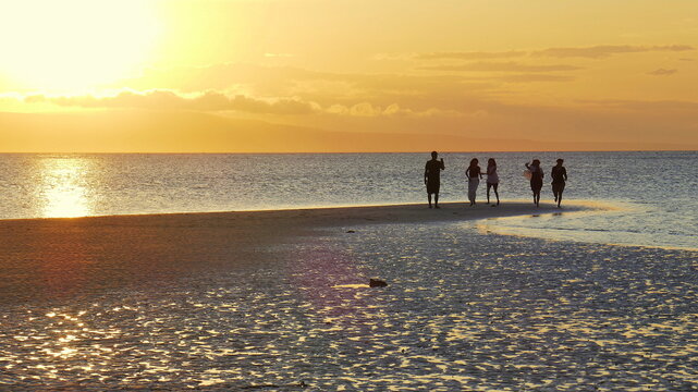 Die Sonne senkt sich malerisch am Walakiri Strand auf der Sumba Insel hinter 5 Personen als Silhouetten und zeichnet Strukturen im feuchte Sand