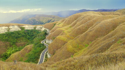 Schöne Landschaft nahe Waingapu in Sumba mit braunen grasigen Bergen und kurviger Straße in der Trockenzeit