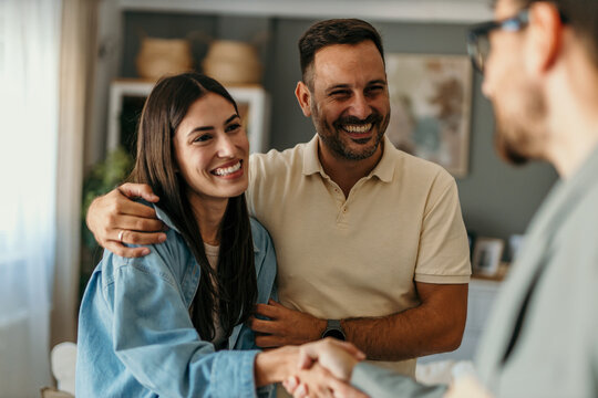 Joyful millennial spouses share a handshake with their therapist at the psychotherapist's office, symbolizing their progress and reconciliation after productive therapy sessions