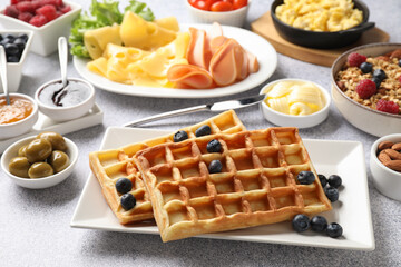 Tasty breakfast. Belgian waffles, blueberries and other food on grey textured table, closeup