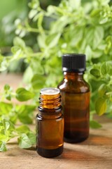 Essential oil in bottles and oregano twigs on wooden table, closeup