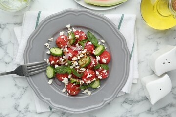 Delicious watermelon salad with feta cheese, vegetables and spices served on white marble table, flat lay