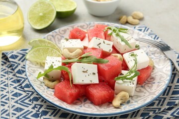 Delicious watermelon salad with feta cheese, cashew nuts and spices served on light table, closeup