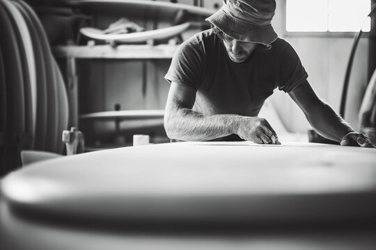 Surfboard shaper crafting a custom board in a coastal workshop.