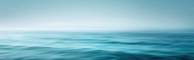 Obraz premium A wide shot of the ocean on a foggy day. The water is a deep blue, with gentle waves rolling across the surface. The sky is a pale blue, blending seamlessly with the sea.