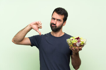 Young handsome man with salad over isolated green wall showing thumb down