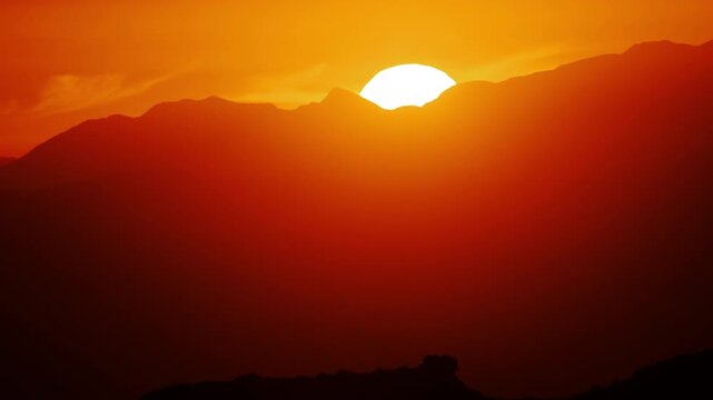 Establishing shot of the sun setting behind the mountain, captured with a handheld camera and slow pan. The gentle motion and warm tones create a peaceful, immersive experience of the golden hour.