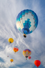Bottom up view to many vivid colorful hot air balloons in sky with light clouds on sunny day