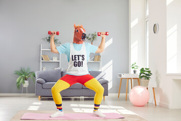 Funny man wearing a horse mask while sport workout at home. With a touch of retro humor, he engages in fitness exercises, lifting dumbbells to stay active and fit in home gym environment.