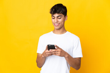 Fototapeta premium Young man over isolated yellow background sending a message or email with the mobile