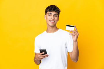 Young man over isolated yellow background buying with the mobile with a credit card