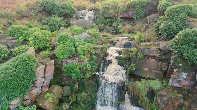 Yorkshire moors host an alluring waterfall. Aerial view reveals water streaming over rocks, falling into a serene blue pool with hikers.