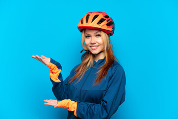 Young cyclist girl isolated on blue background extending hands to the side for inviting to come