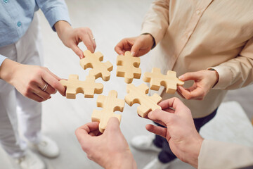 Close up photo hands of people holding diverse pieces of wooden puzzle, team assembling jigsaw...