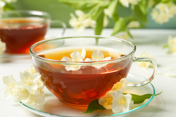 Hot jasmine tea in cup and flowers on white marble table