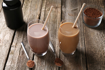 Delicious protein shakes in glasses, powder, spoons and plastic bottle on wooden table