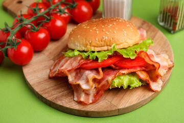 Delicious burger with bacon, tomatoes and lettuce on green background