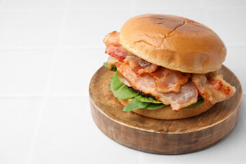 Delicious burger with bacon and greens on white table, closeup. Space for text