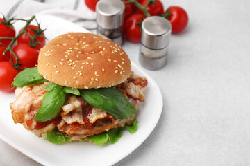 Delicious burger with bacon, greens and tomatoes on light table. Space for text