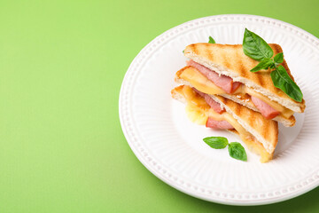Pieces of toasted bread with melted cheese, ham and basil on green background, space for text