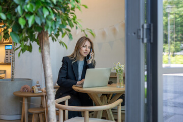 Interested businesswoman hanging on phone online working on laptop while managing contracts in...