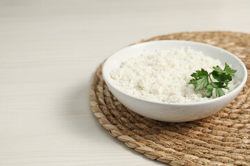 Delicious boiled rice in bowl and parsley on wooden table, space for text