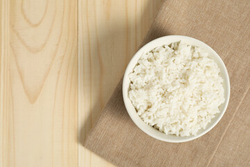 Delicious boiled rice in bowl on wooden table, top view. Space for text