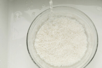 Pouring water into bowl with rice in sink, top view