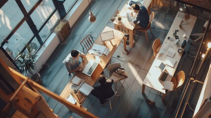 An aerial view of a modern office space with people engaged in work, bathed in natural light streaming through large windows, creating a vibrant, collaborative atmosphere.