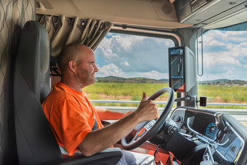 Happy trucker in the cab of a truck while driving with thumb up in OK sign.