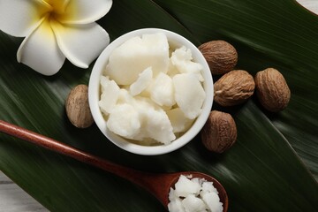 Shea butter in bowl, spoon, flower and nuts on white wooden table, flat lay