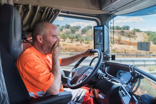 Truck driver driving the truck on the highway and yawning in a clear gesture of tiredness and fatigue at the wheel.
