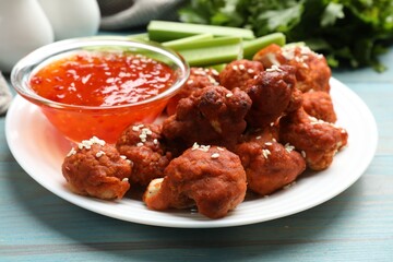 Tasty cauliflower buffalo wings, sauce and celery on light blue wooden table, closeup