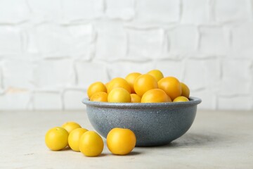 Ripe plums in bowl on light textured table