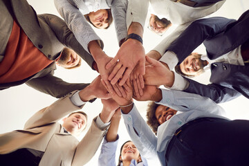 Group of happy multiracial people standing in circle and joining hands as sign of unity and teamwork. Diverse company employees in teambuilding activity, celebrate their success. Low angle, from below