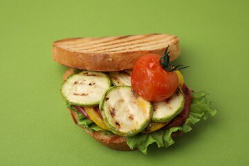 Tasty sandwich with grilled vegetables on green background, closeup