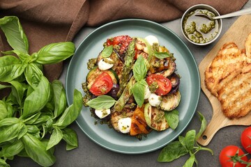 Delicious salad with grilled vegetables, pesto sauce, basil and bread on gray textured table, flat lay