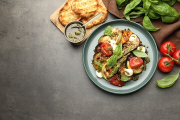 Delicious salad with grilled vegetables, pesto sauce, basil and bread on gray textured table, flat lay. Space for text