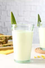 Tasty pineapple smoothie in glass on white wooden table
