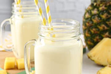 Tasty pineapple smoothie in mason jars and fresh fruit on table, closeup