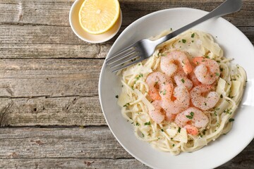 Delicious pasta with shrimps, cheese and lemon on wooden table, top view. Space for text