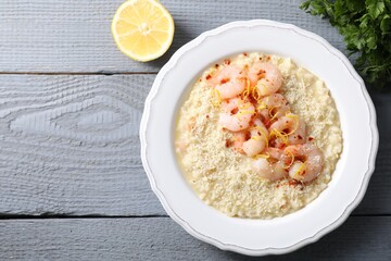 Delicious risotto with shrimps, cheese, lemon and parsley on grey wooden table, top view. Space for text