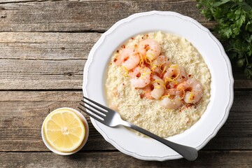 Delicious risotto with shrimps, cheese, lemon and parsley on wooden table, top view